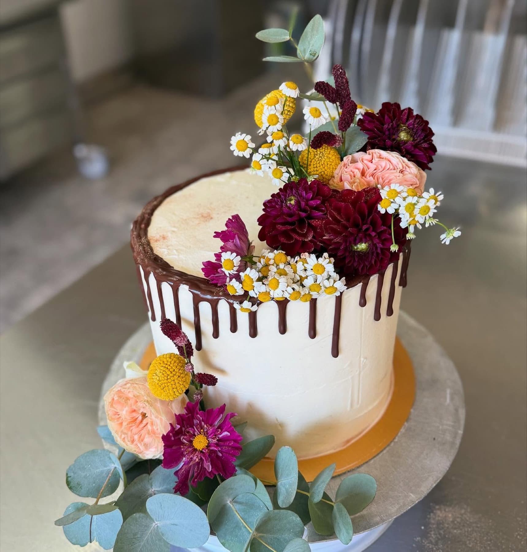 Torte mit Schokoladendrip, bunten Blüten und Eukalyptuszweigen