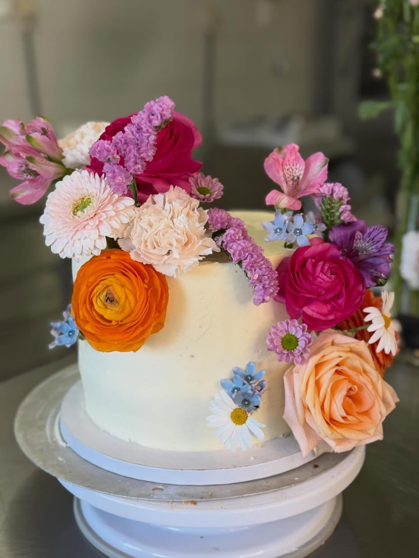 Weiße Torte mit kräftigen Ranunkeln und Rosen in Orange, Pink und Blau