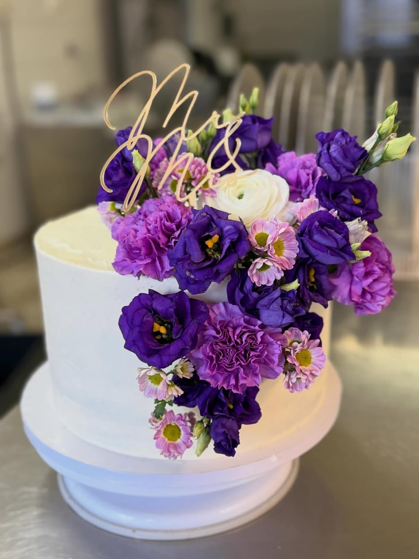 Weiße Hochzeitstorte mit lila Lisianthus und goldenem Mr-and-Mrs-Topper