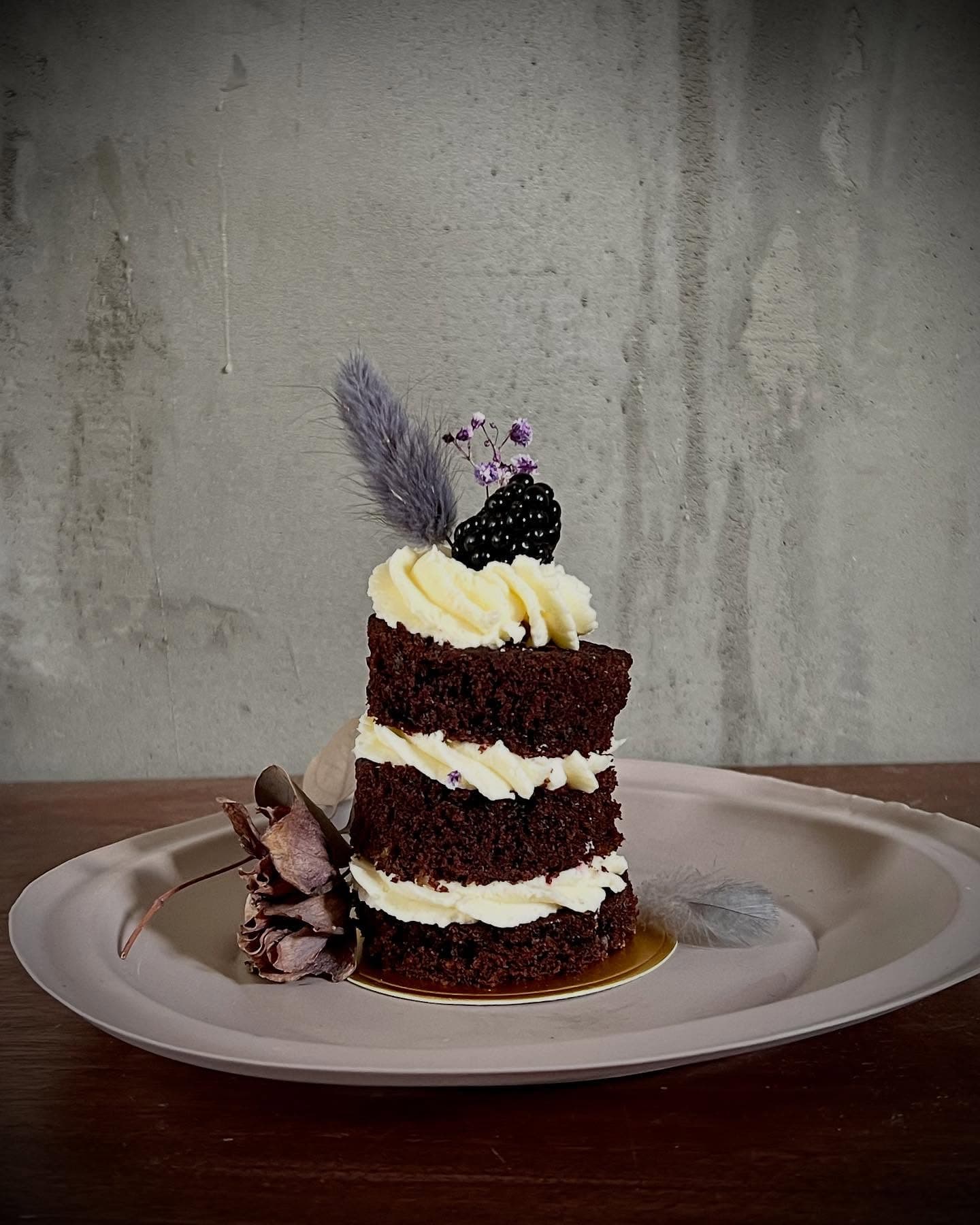 Red-Velvet-Naked-Cake mit Feder und dunkler Deko vor Betonwand