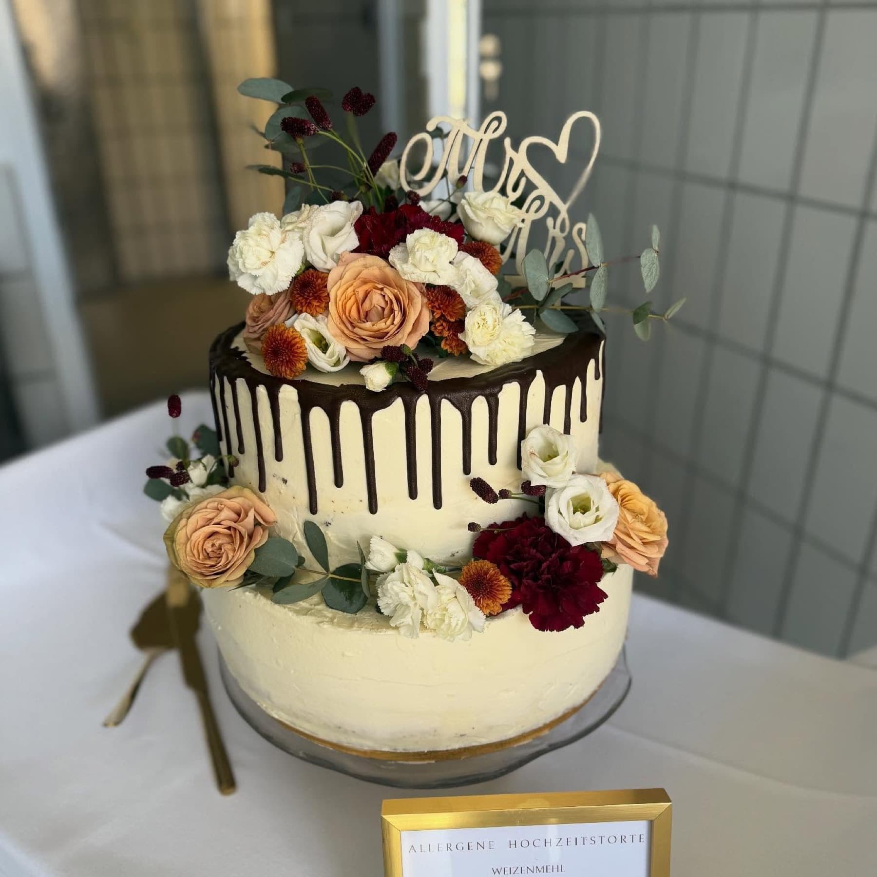 Zweistöckige Hochzeitstorte mit Schokoladendrip und herbstlichen Blüten