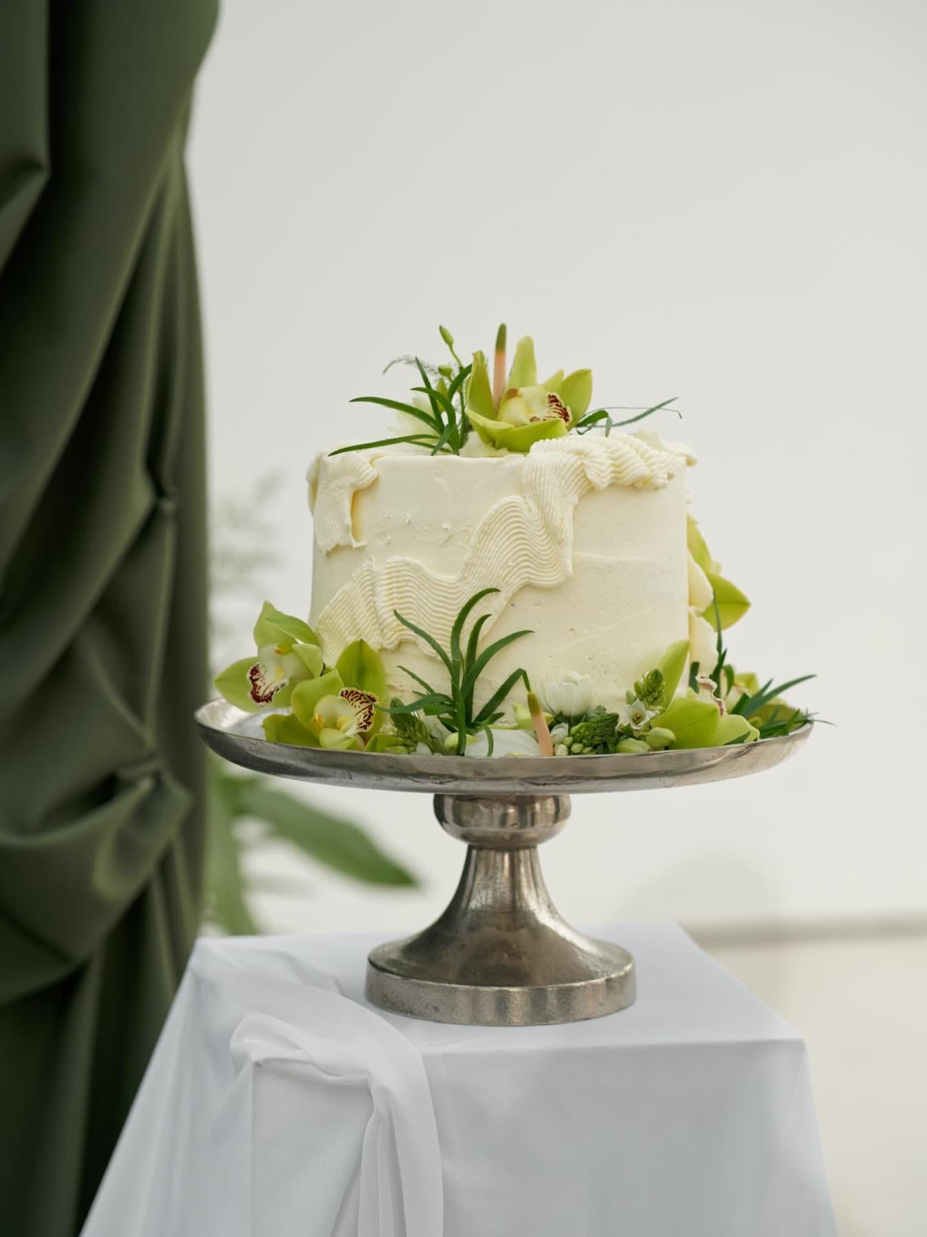 Schlichte weiße Torte mit grünen Orchideen auf silbernem Kuchenständer